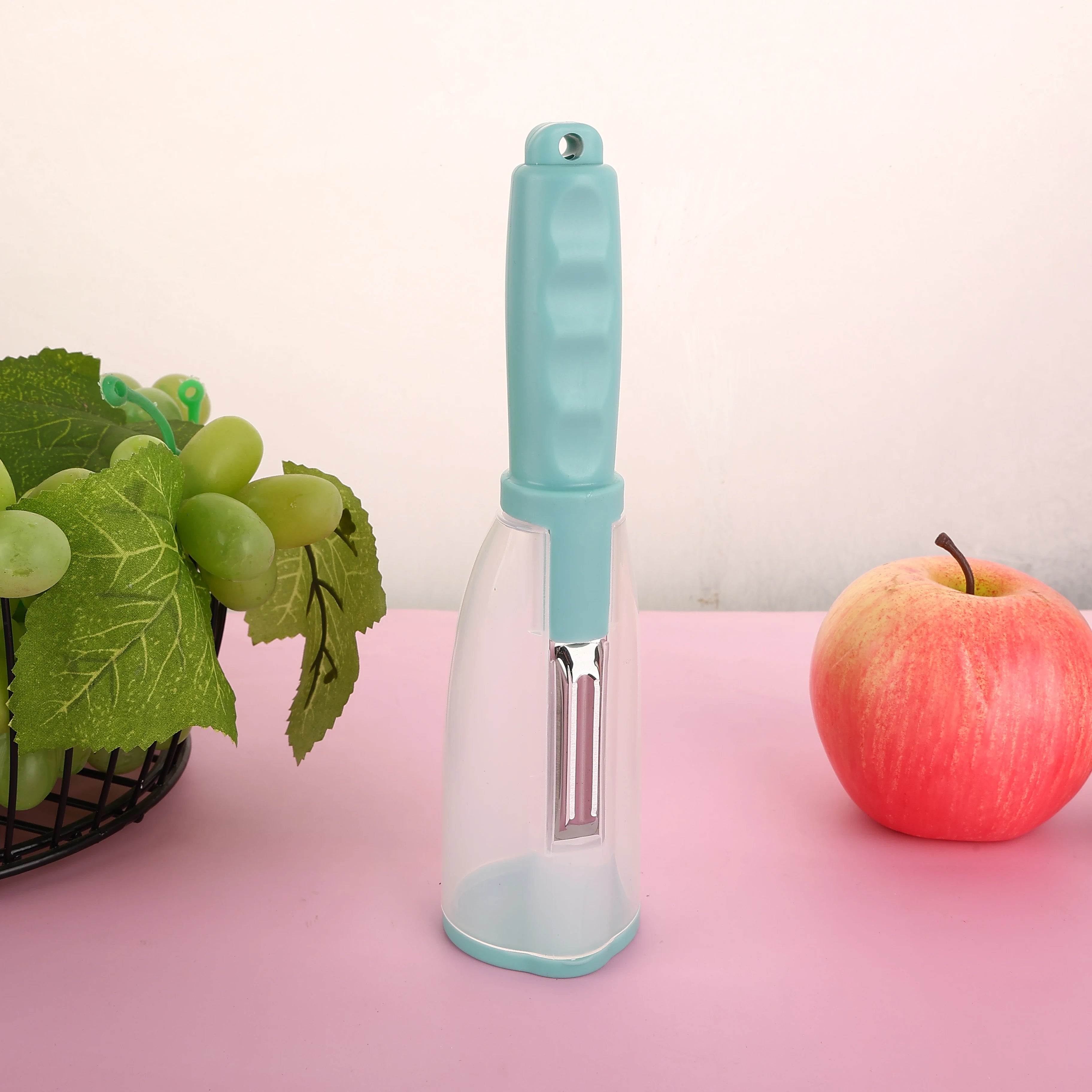 Vegetable Peeler with Container - CozyNest Hub premium handheld tool in green, displayed with fruits on a pink background.