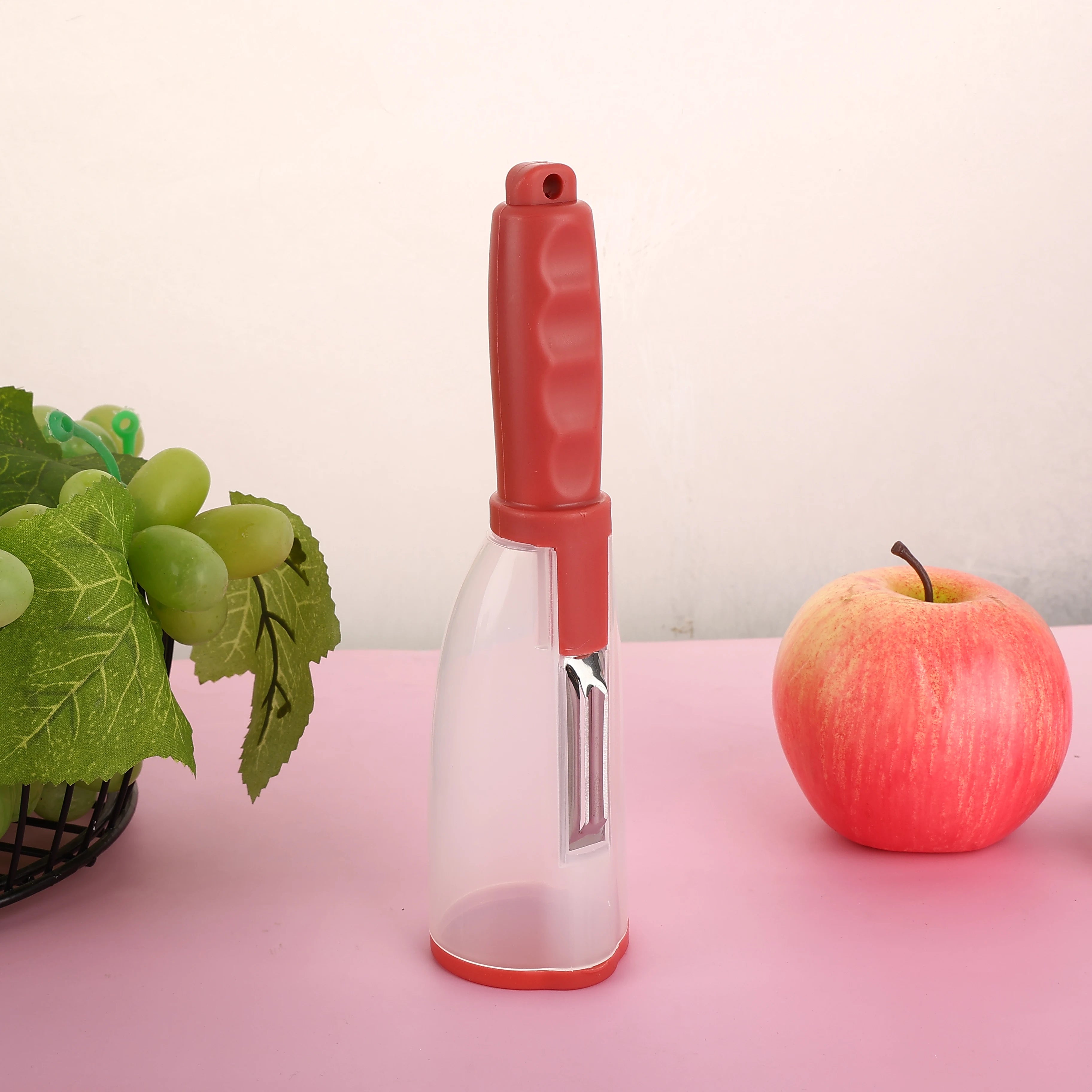 Vegetable Peeler with Container - CozyNest Hub premium handheld tool in green, displayed with fruits on a pink background.