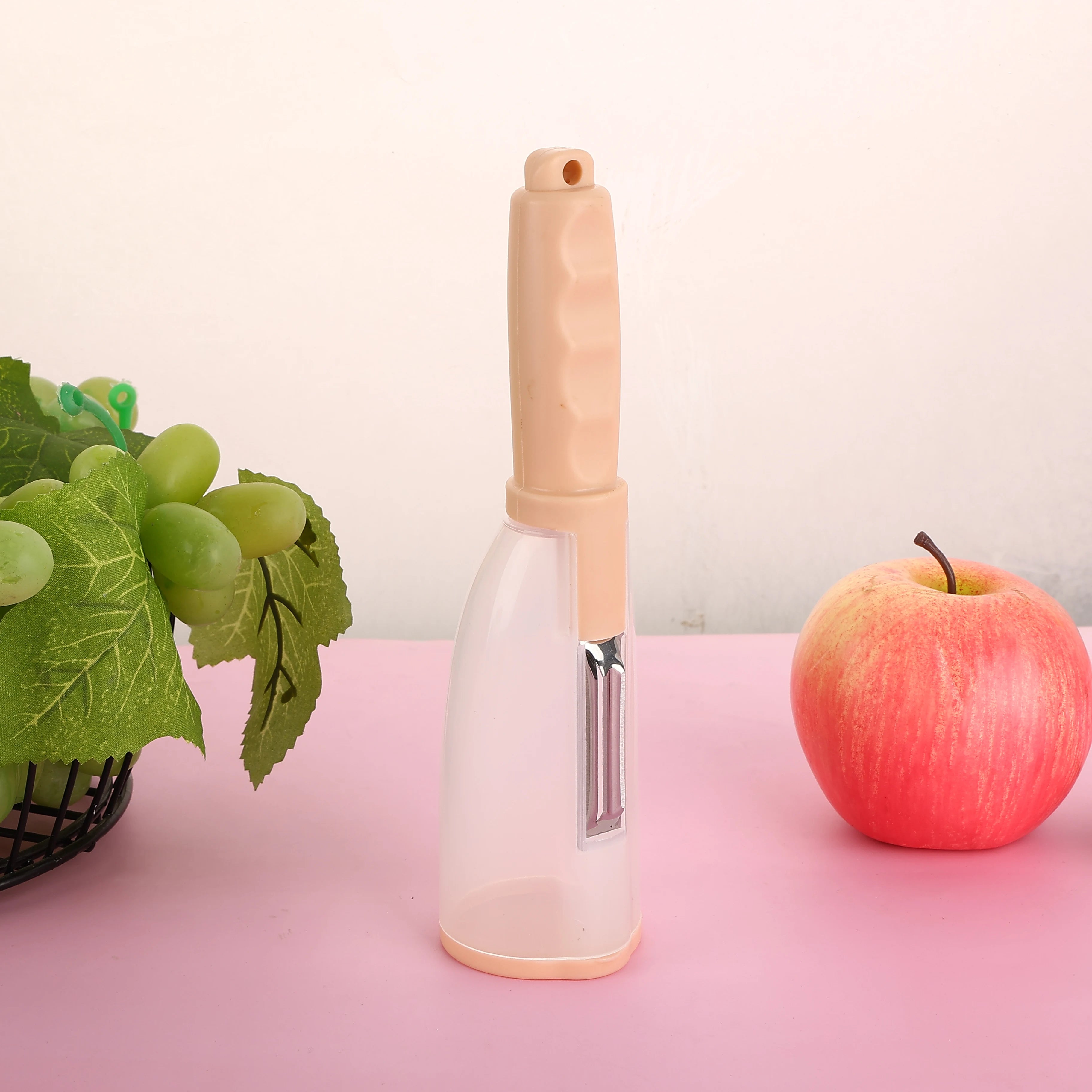 Vegetable Peeler with Container - CozyNest Hub premium handheld tool in green, displayed with fruits on a pink background.